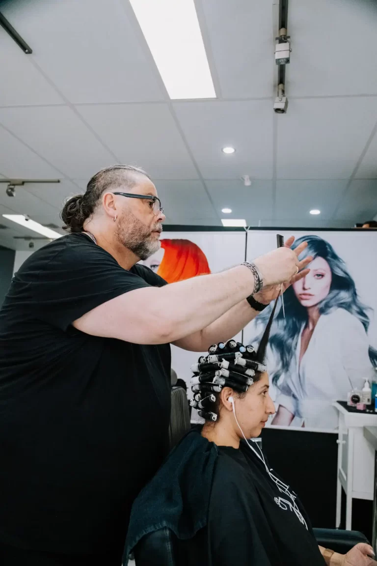 Hairdresser in a black shirt cutting a client's hair in a salon, client seated with curlers in their updo.