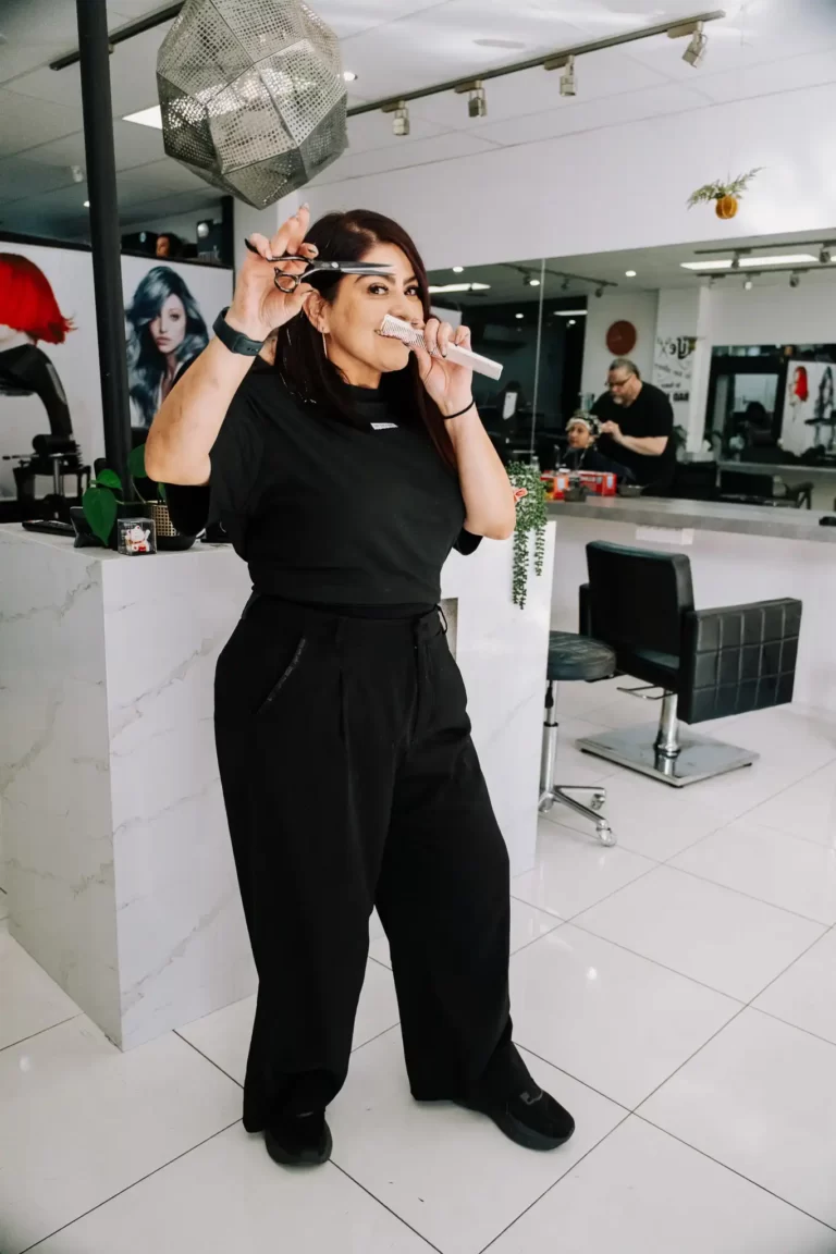 Hairdresser in black cutting a client’s hair with scissors and comb in a bright modern salon with mirrors and chairs in the background