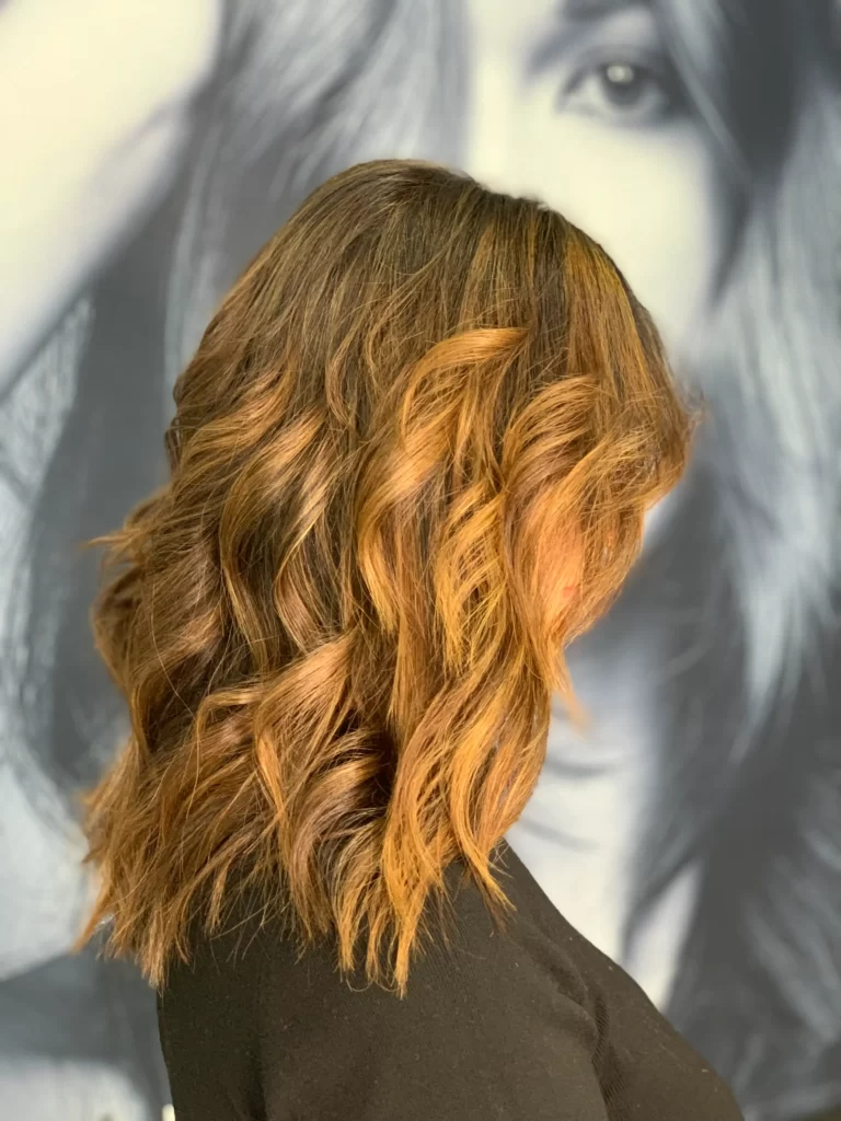 Back of a person with wavy copper hair wearing a black top, standing in front of a large grayscale portrait backdrop.